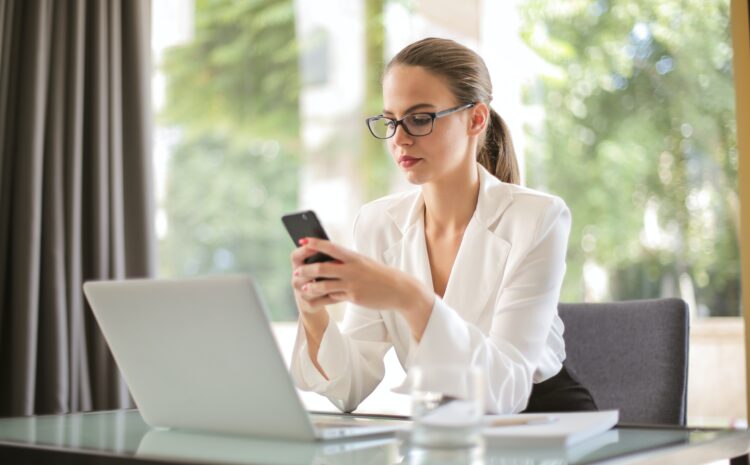 woman holding mobile phone infront of laptop